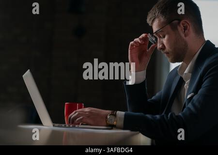 Jeune homme d'affaires dans un costume semble stressé et contemplatif tout en travaillant sur son ordinateur portable. Concept de pression au travail, de prise de décision et de négociation Banque D'Images