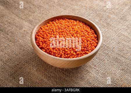 un bol en bois avec des grains de lentilles rouges sur une toile de jute. vue de dessus des lentilles orange séchées à l'intérieur du bol. Banque D'Images