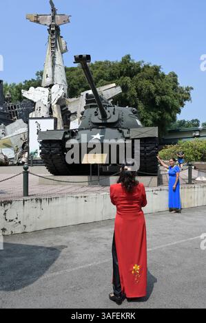 VIETNAM, Hanoi, Musée militaire, matériel militaire et débris de guerre de la guerre coloniale française 1946-1954 et de la guerre américaine au Vietnam 1955 – 1975, char de combat américain M-48 Patton et épave de Grumman F6F Hellcat un avion de chasse américain utilisé par l'armée coloniale française, abattu au combat à Dien bien Phu 1954, une vietnamienne pose pour une photo Banque D'Images
