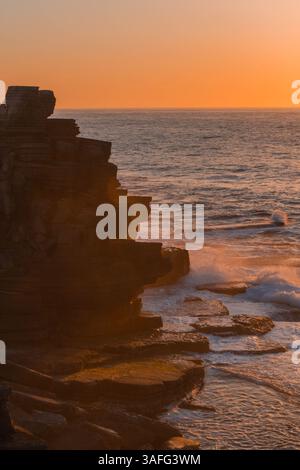 Les couleurs chaudes du coucher de soleil baignent la côte accidentée de Peniche, tandis que les vagues s'écrasent contre les falaises majestueuses, capturant la beauté naturelle et sereine à son meilleur Banque D'Images