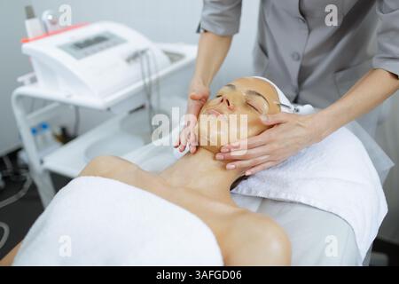 Esthéticienne appliquant le masque facial dans le salon de spa, effectuant des soins de la peau et un traitement du visage pour le rajeunissement. Banque D'Images