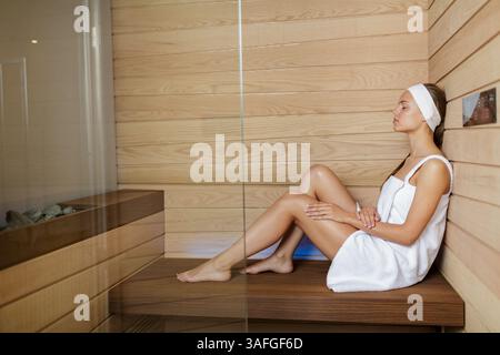 Femme en serviette se relaxant dans une salle de sauna en bois, profitant de la thérapie chaude et retraite de bien-être paisible seul. Banque D'Images