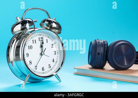 Réveil, livre et écouteurs sur fond bleu clair Banque D'Images