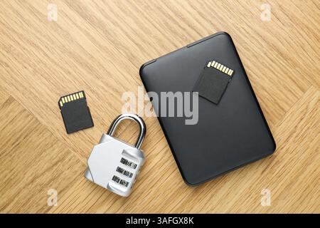 Disque dur externe, cartes mémoire SD et cadenas à combinaison sur table en bois clair, plat Banque D'Images