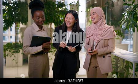 Divers collègues multiraciaux heureux partenaires d'affaires afro-asiatiques musulmanes femmes d'affaires souriantes filles riantes collègues dans le bureau bavardant parler Banque D'Images