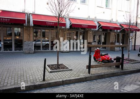 Lviv, Ukraine - 06 avril 2025 : vue extérieure d'un café avec des auvents rouges et un scooterin rouge garé à Lviv, Ukraine. Banque D'Images
