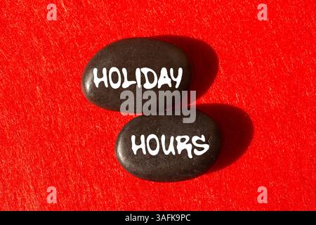 Message d'heures de vacances écrit sur des pierres noires sur fond rouge. Symbole conceptuel des heures de congé. Copier l'espace. Banque D'Images