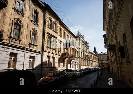 Lviv, Ukraine - 06 avril 2025 : Rue européenne à l'architecture historique, voitures garées et lumière chaude du soleil à Lviv, Ukraine. Banque D'Images