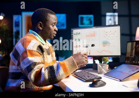 Brandissant de son appartement, homme noir utilisant un ordinateur portable pour participer à des réunions en ligne. Les indépendants masculins utilisent la technologie sans fil pour la visioconférence avec leurs collègues afin de discuter du travail à distance. Banque D'Images