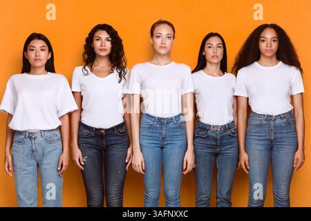 Groupe de cinq femmes multiraciales sérieuses debout sur fond jaune Banque D'Images