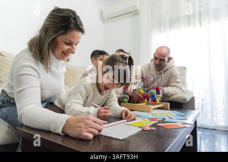 Mère aidant sa fille à dessiner tandis que père et fils jouent avec des jouets dans le salon Banque D'Images
