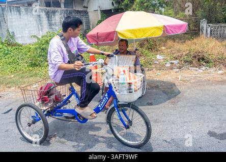 BANGKOK, THAÏLANDE, 13 APR 2024, Une femme sur un tricycle roule autour d'un vendeur de billets de loterie qui est assis dans un fauteuil roulant Banque D'Images