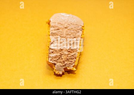 Tranche de gâteau de crème glacée au chocolat reposant sur une croûte de craquelin graham lisse avec un fond jaune vif ajoutant de la chaleur à la composition. Texture crémeuse o Banque D'Images