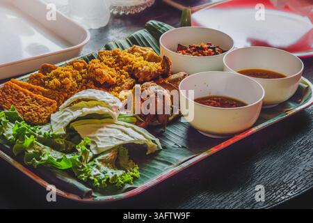 Une portion de poulet frit croustillant accompagné de tempeh, laitue, chou, sauces trempées et sambal, un plat populaire dans le style sundanais des indones Banque D'Images