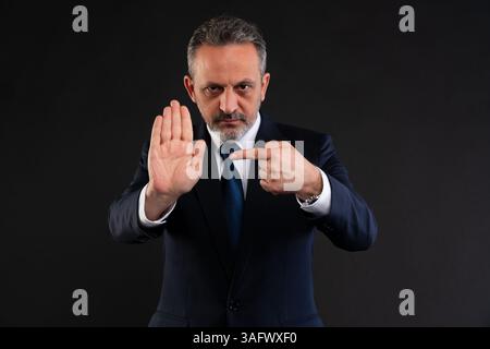 Homme d'affaires confiant en costume tenant sa main dans un geste d'arrêt tout en pointant vers elle, soulignant un avertissement, une règle, ou un refus fort. Banque D'Images