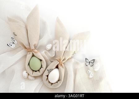Oeufs de Pâques enveloppés dans une serviette pliée comme des oreilles de lapin sur un tissu de lin. Joyeuses Pâques concept. Vue de dessus. Avec de l'espace pour votre texte Banque D'Images