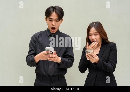 Portrait de jeune couple asiatique portant l'uniforme d'affaires sur fond Uni tout en utilisant le téléphone portable Banque D'Images