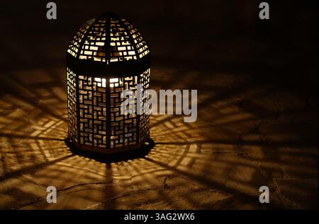 Lanterne traditionnelle projetant des ombres géométriques sur le sol en pierre la nuit Banque D'Images