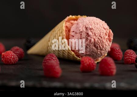 crème glacée à la framboise avec des baies de framboise rouges sur une planche d'ardoise noire, gros plan de la crème glacée aromatisée aux baies avec des framboises fraîches et des mûres Banque D'Images