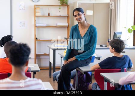 À l'école, enseignante indienne assise sur le bureau et s'engageant avec les élèves en classe Banque D'Images