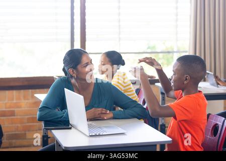 À l'école, enseignante indienne avec ordinateur portable s'engageant avec les élèves dans la discussion en classe Banque D'Images