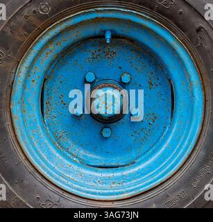 Vue rapprochée d'une roue bleue montée sur un pneu robuste, révélant les surfaces et textures altérées dans un environnement extérieur. Banque D'Images