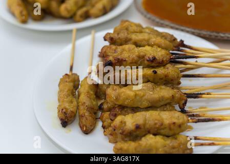 Satay de porc à la sauce aux cacahuètes servi avec des cornichons qui sont des tranches de concombre et des oignons au vinaigre au marché thaïlandais de Street food ou au restaurant à Bangkok T. Banque D'Images