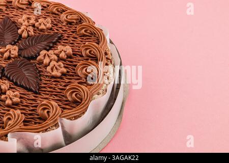 Un gâteau au chocolat magnifiquement conçu présente des motifs de glaçage complexes et des feuilles de chocolat, reposant sur un fond rose doux dans un dessert setti Banque D'Images
