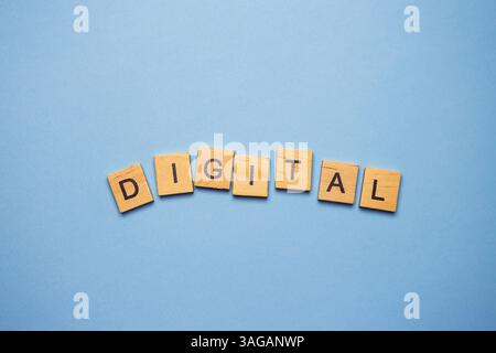 Carreaux de lettres en bois orthographiant le mot « DIGITAL » disposés sur un fond bleu clair. Banque D'Images