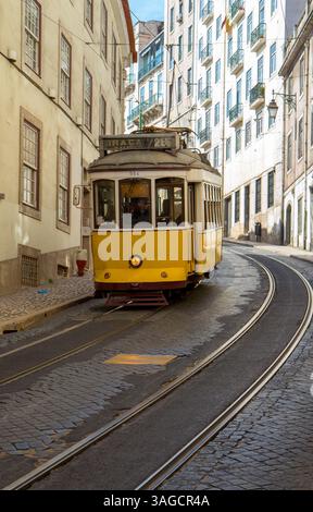 Le tramway jaune historique numéro 28 traverse une rue étroite de Lisbonne, Portugal. Symbole classique du charme de la ville, les transports en commun traditionnels Banque D'Images