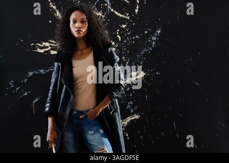 Femme confiante en Jean déchiré et veste en cuir debout contre le mur éclaboussé. Mode, style, confiance, edgy, urbain, tendance Banque D'Images