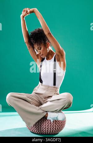 Femme à la mode s'étirant sur un pouf, portant des bretelles et un pantalon élégant. vêtements, style, tendance, accessoires, élégant, sophistiqué Banque D'Images