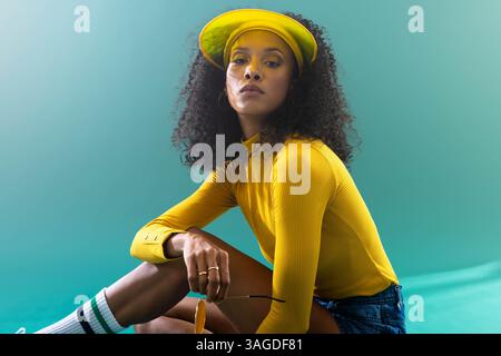 Tenant des lunettes de soleil, femme en haut jaune et visière assis, l'air déterminé. Mode, accessoire, décontracté, confiant, style de vie, loisirs Banque D'Images