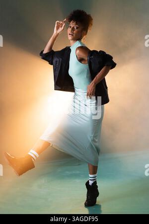 Femme à la mode dans une tenue élégante dansant énergiquement dans un éclairage de studio vibrant. style, danse, coloré, expression, tendance, mouvement Banque D'Images