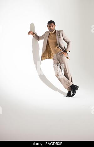 Homme élégant en costume beige posant en toute confiance contre le mur blanc du studio. Mode, confiance, hommes, élégance, style, portrait Banque D'Images