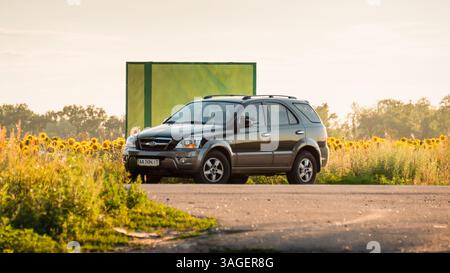 SUV noir garé sur un côté de la route dans le champ de tournesol. Kia Sorento sur le bord de la route près d'un panneau vert vide. Banque D'Images