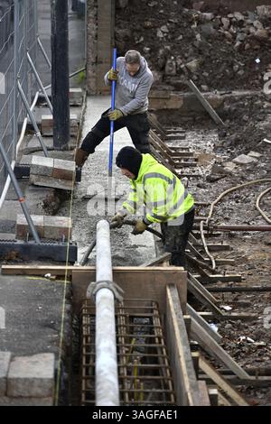Constructeurs nivelant le béton pompé entrant dans la poutre renforcée en acier à coffrage en bois et compactant avec la machine vibrante sur le chantier de construction Banque D'Images