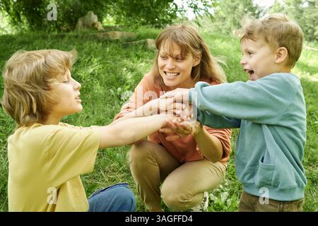 Mère souriante jouant avec deux fils dans le parc Banque D'Images