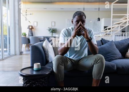 Homme afro-américain réfléchi assis sur le canapé à la maison, contemplant avec les mains ensemble. Méditation, relaxation, pleine conscience, concentration, thinki Banque D'Images