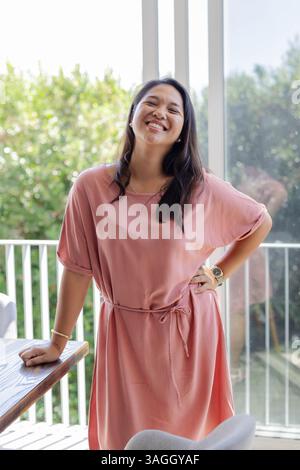 Femme souriante en robe rose profitant d'une journée ensoleillée au bord de la piscine à la maison. Été, loisirs, luxe, détente, vacances, bonheur Banque D'Images