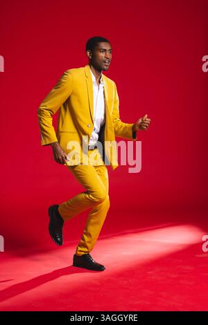 Homme confiant en costume jaune posant énergiquement sur fond rouge vif. Mode, style, confiance, audacieux, vêtements pour hommes, portrait Banque D'Images