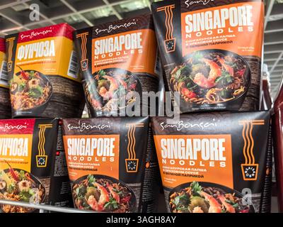 Bobruisk, Biélorussie - 10 mars 2025 : des emballages de nouilles aux couleurs vives présentent des nouilles de Singapour remplies de légumes et d'épices. Banque D'Images