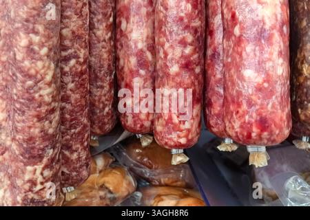 Des saucisses de chorizo rouge vif pendent des crochets dans un étal de marché animé. Autour des charcuteries sont diverses épices, mettant en valeur la saveur vibrante Banque D'Images