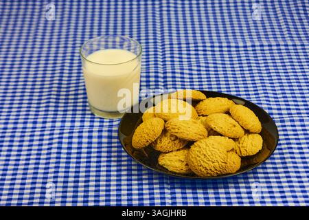 Une assiette de biscuits repose sur une nappe à carreaux bleue et blanche à côté d'un verre de lait. Les biscuits sont disposés en forme de pyramide, avec le dessus Banque D'Images