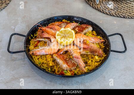 Vue de haut en bas d'une paella traditionnelle aux fruits de mer servie dans une poêle en fonte, garnie de crevettes, de poisson et d'une tranche de citron frais. Cuisine espagnole à son Banque D'Images