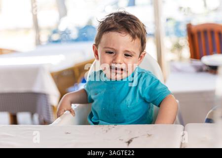 Bébé garçon pleurant en mangeant du riz noir dans une chaise haute Banque D'Images