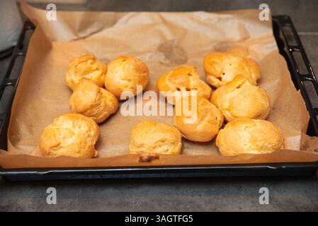 Bouffées à la crème brun doré reposant sur du papier cuisson après avoir été fraîchement cuites, prêtes à être remplies de garnitures sucrées ou salées. Banque D'Images