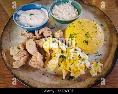 Cuisine traditionnelle moldave, repas en gros plan avec ragoût de porc, polenta mamaliga, œufs frits, fromage et crème sure saupoudrée de persil Banque D'Images