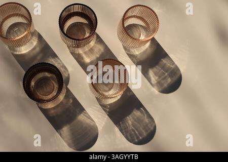 Placez des verres colorés en verre brun et beige avec de l'eau à la lumière du soleil. De belles ombres. Concept de nature morte d'été. Boisson pour les événements, vin blanc Banque D'Images