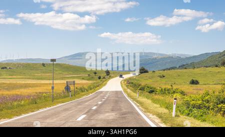 Route en Bosnie-Herzégovine, Europe. Route pittoresque à travers des collines vallonnées menant à des montagnes lointaines sous un ciel bleu vibrant avec cl dispersé Banque D'Images